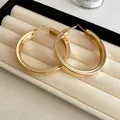 Detailed close-up view of elegant large gold hoop earrings displayed in a cream jewelry box - Smooth (Small) / Gold