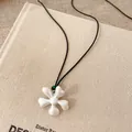 Detail view of a matte white flower pendant necklace with green ceramic beads on a black cord - Flower