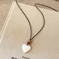 Close-up of a white heart pendant necklace featuring a black leather cord and stone beads. - Heart