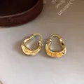 Detailopname van gouden U-vormige oorbellen met een unieke gehamerde geplooide textuur. - Oorringen-Goud