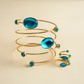 Detail eines zweiteiligen goldfarbenen Spiralarmbands und Rings mit blauen Steinen. - Gold Mit Blauem Stein Set
