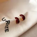Detailopname van rode emaille oorbellen met polkadots in C-vorm op een linnen achtergrond - Oorspeld Stijl / Goud-Rood