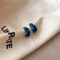 Gedetailleerde weergave van blauwe C-vormige oorknopjes met witte stippen op tas - Oorspeld Stijl / Goud-Blauw