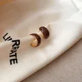 Detailweergave van bruine emaille C-vormige oorringen met witte stippen op een stoffen zak. - Oorspeld Stijl / Goudbruin
