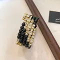 Detailopname van een gelaagde gouden armband met zwarte kralen en glinsterende stras - Goud-Zwart