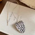 Detailansicht einer Halskette mit Leopardenmuster-Anhänger und Brillenclip auf Textur. - Halskette / Beige-Schwarz Leopard