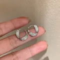 Sparkling zircon twisted hoop earrings with 14k white gold plating shown on fingers for scale - Twisted Hoop / Silver
