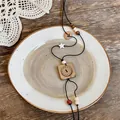 Macro detail of retro wooden square pendant necklace displayed on a rustic ceramic plate - Square Plaque Pendant / Brown