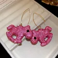 Close-up view of pink rhinestone-encrusted pony-shaped drop earrings presented in jewelry box - Gold Pink