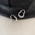 Makro-Detail von silbernen, unregelmäßig gewellten C-Ohrringen mit Falten-Textur-Design - Silber Plissiert Ohrclip Stil / Silber