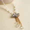 Gedetailleerde opname van een elegante ketting met bladhangers en gouden kettingkwastjes - Ketting / Wit / Goud