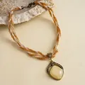 Detailopname van een vintage gevlochten ketting met een hanger van hars en fonkelende strass. - Gouden Gele Ruit Stijl