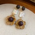 Detailed close-up view of bohemian woven straw flower drop earrings with wooden and marbled beads - Silver / Brown