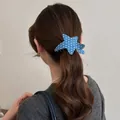 Detail view showing a stylish blue star-shaped acetate hair claw clip used on a ponytail. - Silver Star / Blue Star Pattern