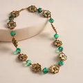 Detail view of a vintage-style metal flower necklace with green resin beads on a display. - Necklace / Antique Gold-Emerald Green
