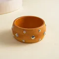 Close-up detail of a wooden ethnic bangle with silver geometric metal rivets. - Light Coffee
