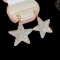 Gros plan de boucles d'oreilles pendantes en étoile avec strass blancs brillants - Grande Forme d'Étoile Couleur AB / Crochet d'Oreille Doré