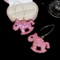 Gros plan de boucles d'oreilles cheval à bascule en strass roses et cristaux étincelants - Forme de Cheval à Bascule Rose / Crochet d'Oreille Doré