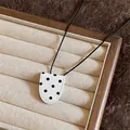 Close-up detail of a minimalist leather polka dot pendant necklace on a jewelry tray - Necklace / White