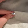Detailed view of a round zircon ring with side stone clusters held by a hand. - Silver