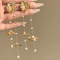 Detalle de pendientes de borla de flores doradas con cuentas y brillo metálico. - Dorado
