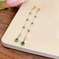 Detail shot of elegant long tassel earrings with green zircon stones on a cream surface. - Long Tassel Stud Earrings (HE35674) / Gold-Green