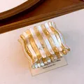 Detailaufnahme eines zweifarbigen gewellten Metall-Stretcharmbands auf beigem Display - Gold-Silber