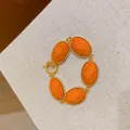 Close-up detail of the vibrant orange resin oval bracelet with gold finish metal facets - Orange
