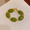 Close-up of vintage style bracelet with green oval resin and gold toggle clasp. - Green