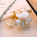 Detailansicht der goldfarbenen Blumenmanschette und des Rings mit weißer Emaille-Textur - Ring Und Armband Set / Gold-Weiß