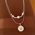 Nahaufnahme einer silbernen Doppelkette mit Gänseblümchen-Anhänger und weißen Perlen - Silber-Gold Mix