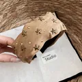 Detalle de una diadema de tela caqui vintage con tachuelas metálicas decorativas de estrella. - Diadema Café Claro