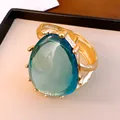 Auffälliger goldfarbener Armreif mit einem großen, durchscheinenden blaugrünen Harzstein - Armband-Gold-Blau