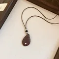 Gedetailleerd overzicht van een retro druppelhanger ketting aan een bruin leren koord. - Zwart/Koffie