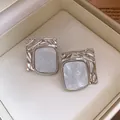 Close-up detail of silver-toned wrinkled square stud earrings with marble texture - Silver