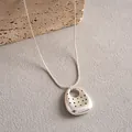 Dettaglio di una collana d'argento con un pendente traforato a pois dal design unico. - Ovale / Argento
