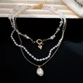 Detailopname van elegante drielaagse parelketting met hart- en schelpachtige hangers - Ketting (Set van 3) / Goud