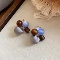 Gedetailleerde weergave van handgemaakte oorbellen met grijze stoffen bollen en hout - Blauw En Bruin
