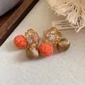 Detailopname van stijlvolle zirkoon bloemoorbellen met oranje en bronzen stoffen bolletjes - Bruin