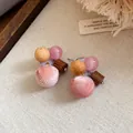 Detailopname van roze pompon oorknopjes met houten kralen en glanzende accenten - Roze Bruin
