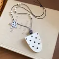 Close-up of a white polka dot leather glasses holder necklace with star charm on a book - White