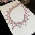 Gros plan d'un délicat collier de perles de cristal violet tissé sur un coffret blanc - Collier-Violet