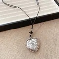 Gros plan d'un pendentif en forme de cœur gravé sur un cordon en cuir noir épuré - Collier Pendentif Coeur Imprimé / Argent-Noir