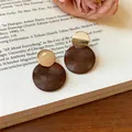 Nahaufnahme von retro Holz- und Gold-Geometrie-Ohrhängern auf einem offenen Buchhintergrund - 2# Runder Stil (HE35690) / Silbernadel / Goldbraun