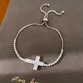 Close-up van zilveren kruisarmband met zirkonia steentjes op getextureerde achtergrond. - Kruis Stijl (5#)