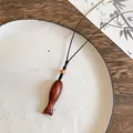 Detailaufnahme einer handgefertigten Holzhalskette mit Fischanhänger auf einem Keramikteller - Ovaler Kleiner Fisch (Perlen) / Braun