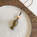 Nahaufnahme einer handgefertigten Fisch-Halskette aus Holz auf einem minimalistischen Teller - Basisstil / Hellkaffee