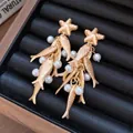 Detail view of gold starfish earrings with pearl-decorated fish tassels in a black box - Silver Pin-Gold-White