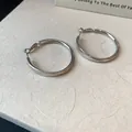 Nahaufnahme von minimalistischen polierten silberfarbenen Creolen auf Texturhintergrund - Glatter Runder Creolen-Stil / Silber