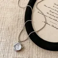Gros plan détaillé d'un collier pendentif montre ronde en argent sur fond de toile - Rond / Argent